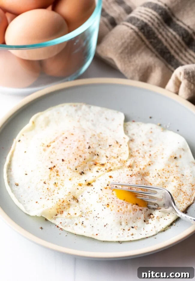 Mastering Over Easy Eggs 4 Fork cutting into the soft yolk of a gently over easy fried egg, on a light blue plate.
