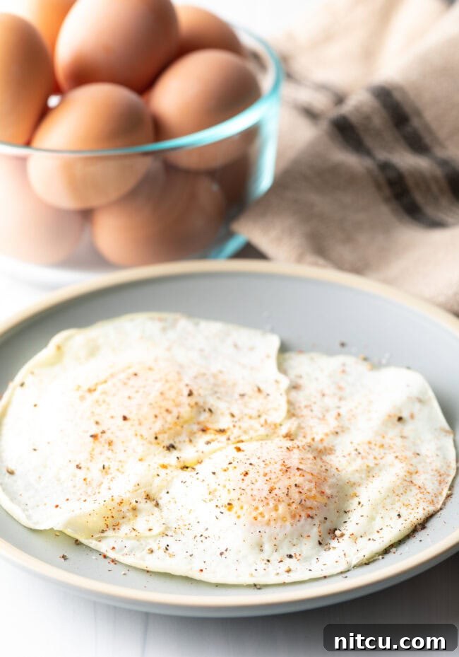 Mastering Over Easy Eggs 5 Two cooked eggs over easy on a light blue plate, sprinkled with spices.