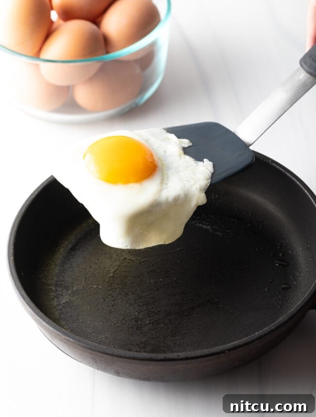 Mastering Over Easy Eggs 9 Flipping a fried egg with a black spatula over a black skillet.