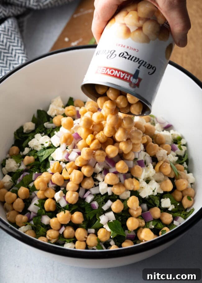 Jennifer Aniston's Go-To Bulgur Salad 8 Can of chickpeas being dumped into the large white bowl with other ingredients.
