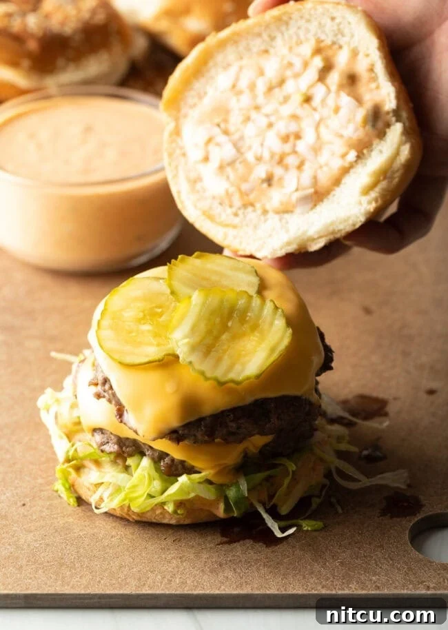 A hand carefully adds the top bun to a fully stacked burger, completing the homemade Big Mac assembly.
