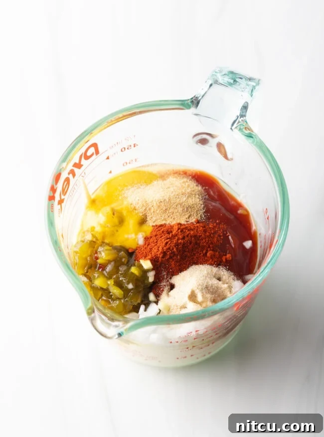 Glass measuring pitcher containing a vibrant mix of ketchup, mustard, mayonnaise, pickle relish, and various spices, prepped for blending into Big Mac sauce.