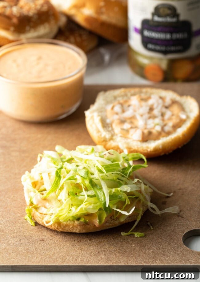 Two halves of hamburger buns, one topped with shredded lettuce and the other with Big Mac sauce, demonstrating the first layers of the burger assembly.