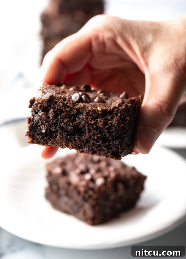 Glow-Up Protein Brownies 4 A hand holding a fudgy protein brownie to the camera, showcasing its moist interior and tempting texture.
