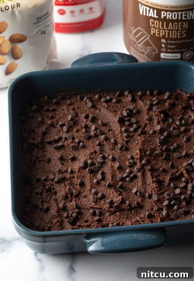 Glow-Up Protein Brownies 8 Brownie batter spread into a square baking pan, topped with chocolate chips, ready for the oven.