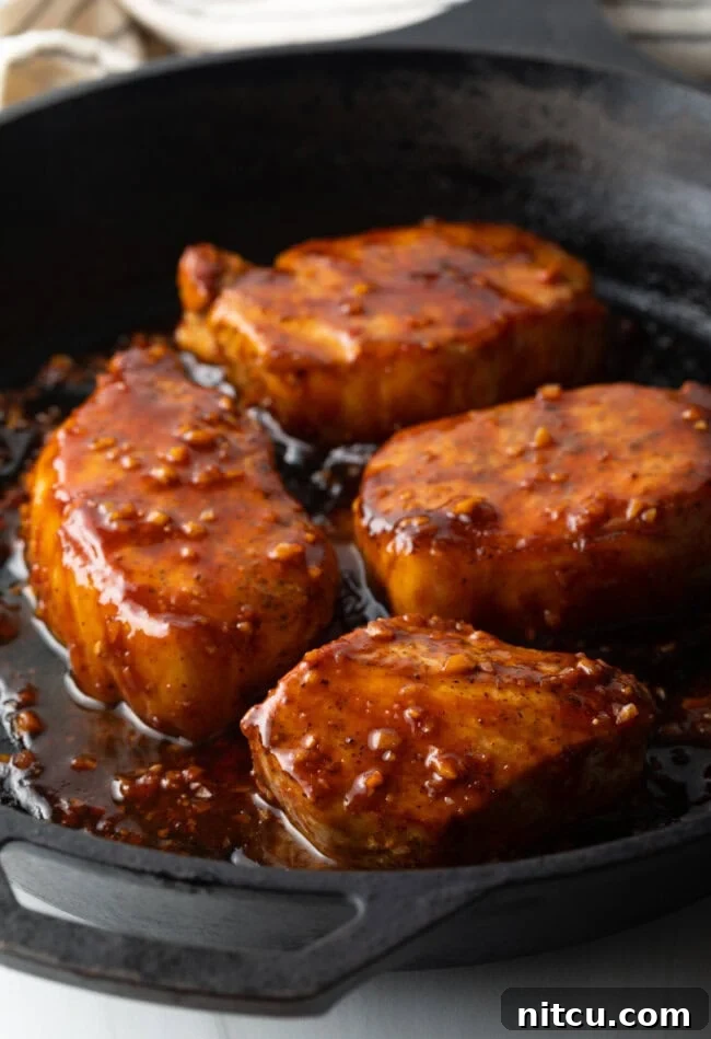 Four perfectly seared pork chops glistening with a rich honey garlic glaze in a black cast iron skillet.