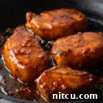 Four delicious honey garlic pork chops in a black cast iron skillet, covered in a sticky, savory-sweet glaze.