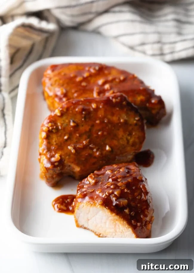 Three perfectly cooked honey garlic pork chops on a white rectangular plate, showcasing the rich, sticky glaze and a cross-section of tender meat.