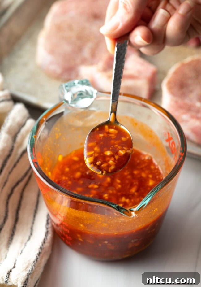 A glass measuring pitcher filled with the perfectly blended spicy honey garlic sauce, with a metal spoon holding a spoonful up to the camera.