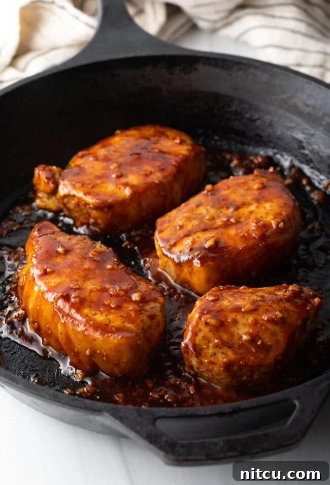 A top-down view of four succulent pork chops immersed in a rich, sticky honey garlic glaze within a cast iron skillet.