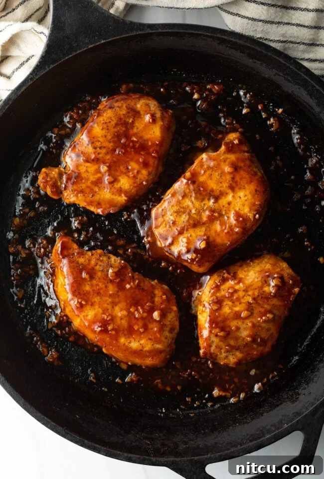 A close-up, top-down view of four honey garlic pork chops, richly coated in glaze, resting in a black cast iron skillet.