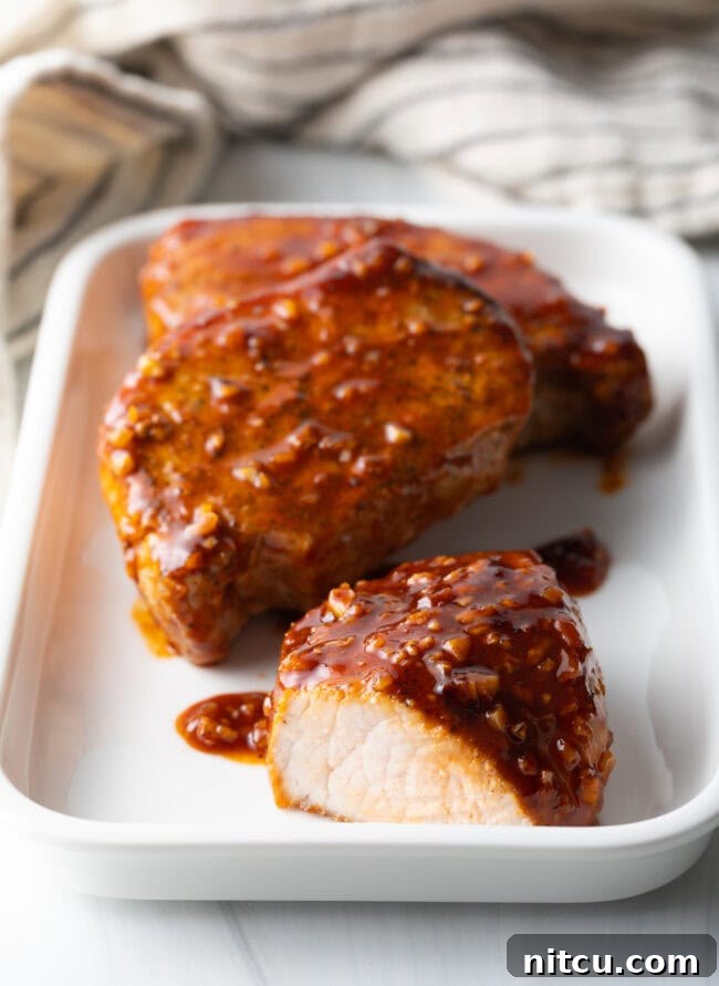 Three honey garlic pork chops plated, one sliced open to show the tender, juicy meat and the glistening, sticky glaze.
