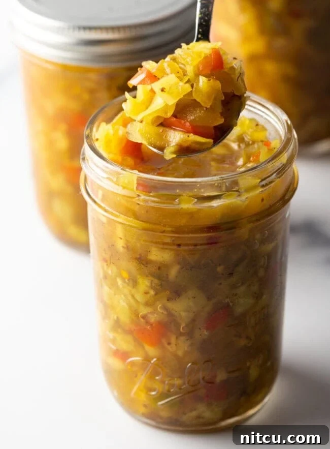 Tangy Homemade Chow Chow 2 Glass jar of southern chow chow recipe. The lid is off and to the right side, a metal spoon is in the jar showing a scoop to camera.