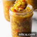 Tangy Homemade Chow Chow 14 Glass jar of southern chow chow. The lid is off and to the right side, a metal spoon is in the jar showing a scoop to camera.
