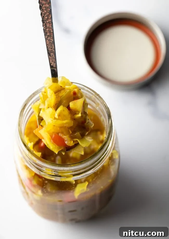 Tangy Homemade Chow Chow 3 Top down view glass jar of chow chow relish. The lid is off and to the right side, a metal spoon is in the jar showing a scoop to camera.