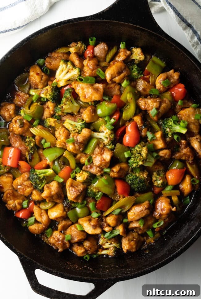 Hunan Firecracker Chicken 12 A close-up view of the delicious chicken and vegetable stir-fry, glistening with Hunan sauce in a cast iron skillet, highlighting its rich textures and colors.