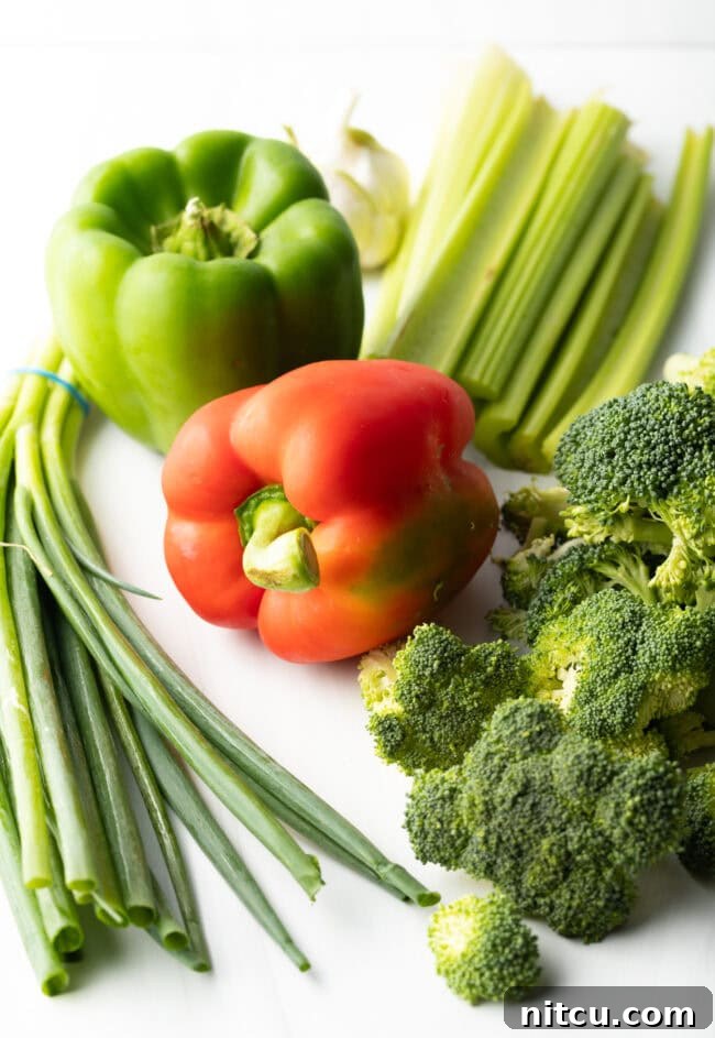 Hunan Firecracker Chicken 4 A vibrant collection of fresh stir-fry ingredients including whole green bell pepper, red bell pepper, crisp scallions, tender celery, and healthy broccoli florets, perfectly prepped for cooking.