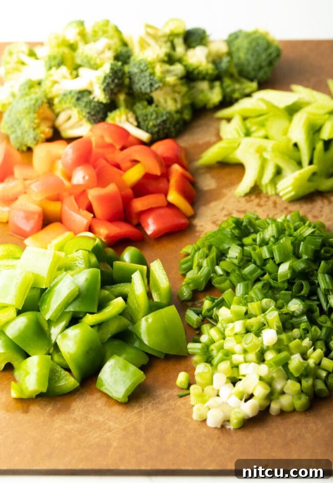 Hunan Firecracker Chicken 5 A cutting board laden with neatly organized piles of chopped green bell pepper, red bell pepper, scallions, celery, and broccoli florets, showcasing precise preparation.