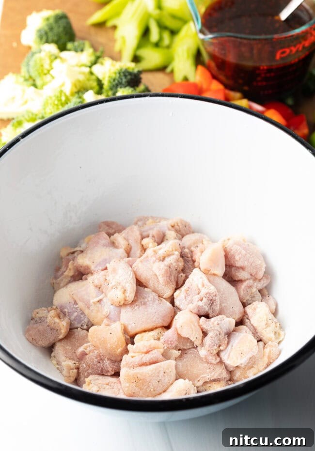 Hunan Firecracker Chicken 6 Raw, neatly chopped boneless chicken thigh pieces are coated with seasonings in a clean white mixing bowl, ready for cooking.