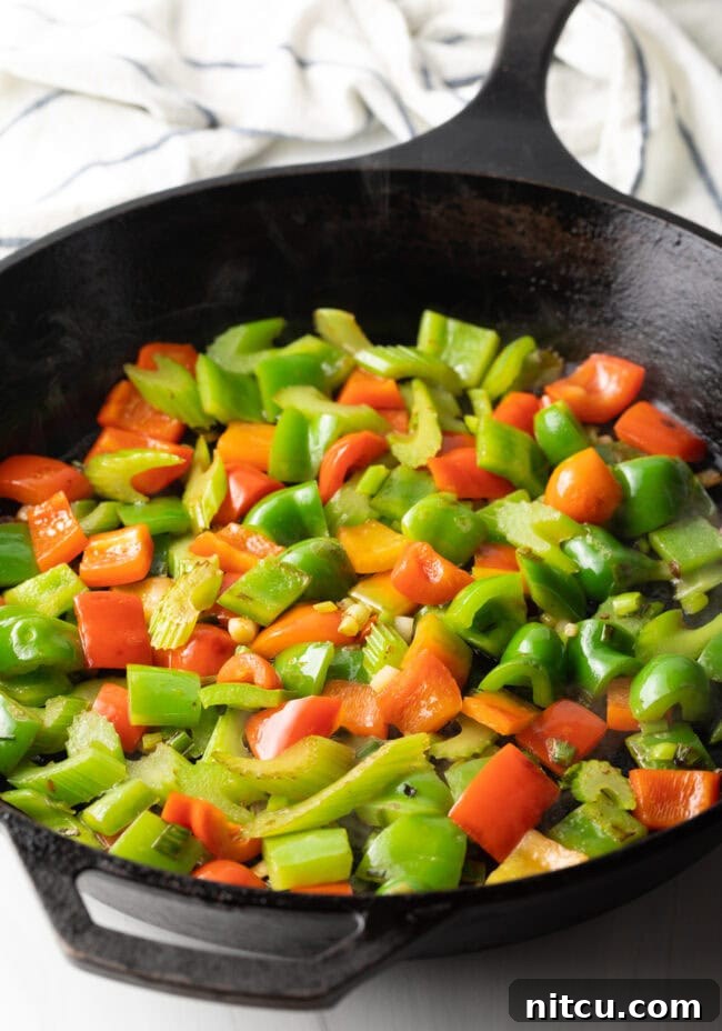 Hunan Firecracker Chicken 8 Vibrant chopped red and green bell peppers are stir-frying in a cast iron skillet, adding color and flavor to the dish.