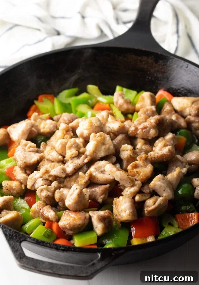 Hunan Firecracker Chicken 9 Cooked chicken pieces are being added back into the skillet with sautéed vegetables, ready to be coated in the sauce.