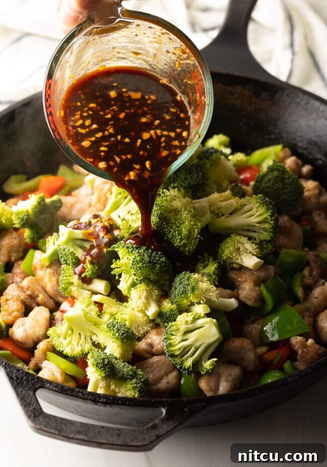 Hunan Firecracker Chicken 10 The savory Hunan sauce is being poured over the colorful medley of chicken and vegetables in a sizzling skillet, creating a rich glaze.