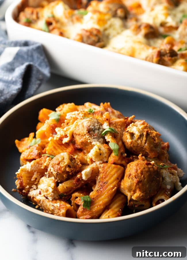 One-Pan Meatball Casserole 11 Dark gray plate with a generous portion of baked meatball casserole with pasta and cheese.