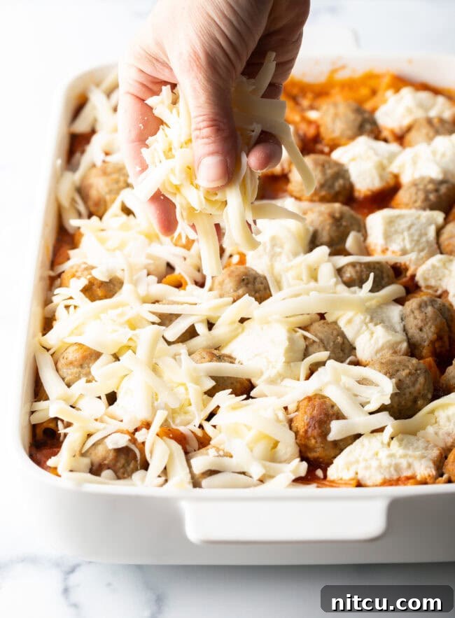 One-Pan Meatball Casserole 8 Hand adding shredded mozzarella to the casserole.