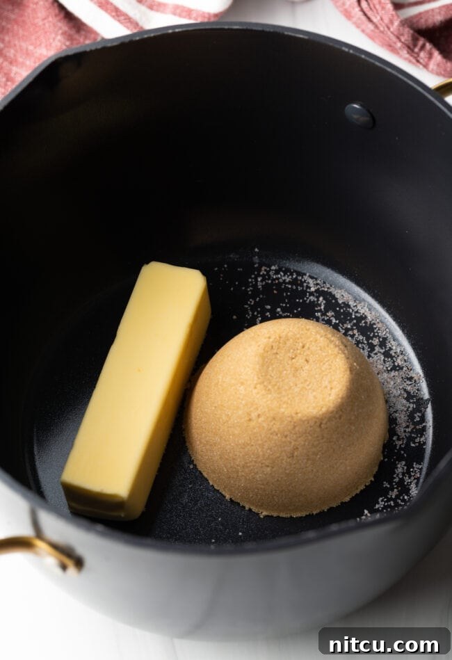Close-up shot of light brown sugar and chunks of butter melting together in a sauce pot over medium heat, starting the caramel making process.
