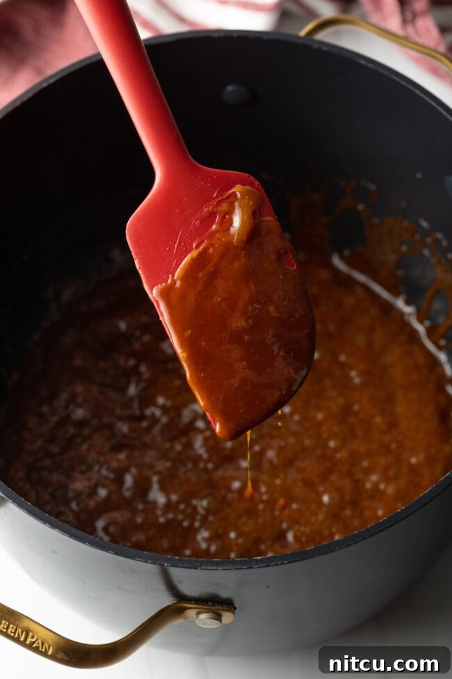 A close-up of the caramel sauce gently simmering in a pot, with a whisk checking its developing thickness and color.