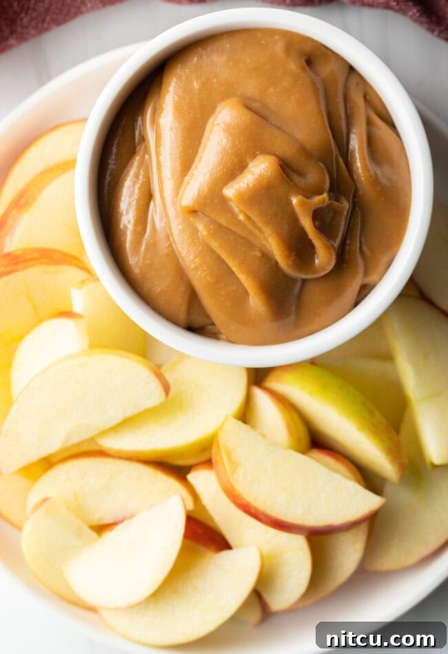 Top-down view of a white bowl filled with cream cheese caramel apple dip, surrounded by an abundant display of fresh apple slices, ready for serving.