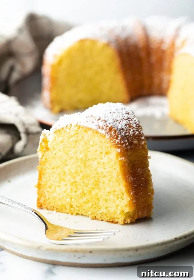 Sun-Kissed Lemon Olive Oil Cake 2 A perfectly baked slice of vibrant yellow lemon olive oil cake, glistening with moisture, presented on a pristine white plate, inviting a taste of its rich citrus aroma and tender crumb.