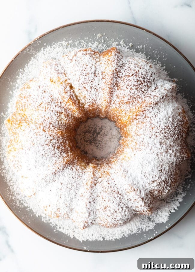 Sun-Kissed Lemon Olive Oil Cake 4 A stunning bundt cake, golden-brown and elegantly dusted with powdered sugar, awaits slicing on a white plate, showcasing the beautiful form achievable with this recipe.
