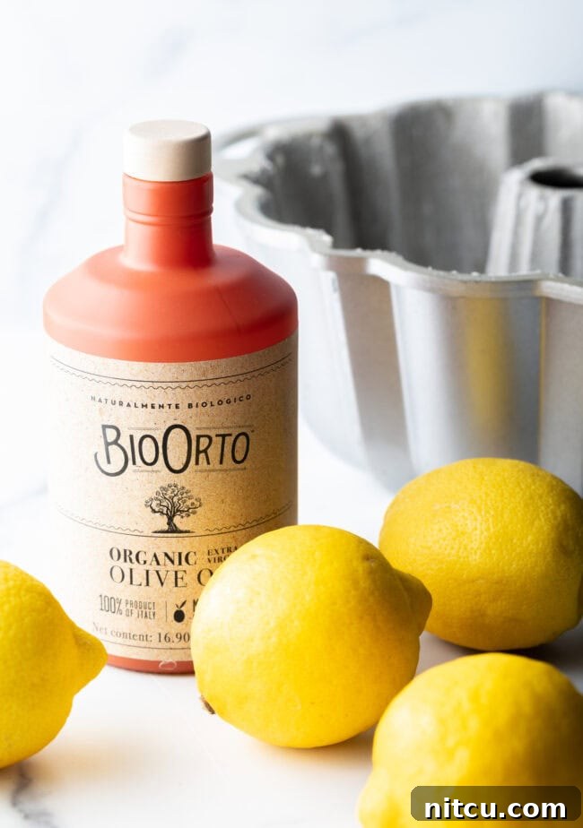Sun-Kissed Lemon Olive Oil Cake 5 The essential ingredients laid out: a bottle of premium olive oil, representing quality, and four bright, fresh lemons, signaling the vibrant citrus heart of the recipe.