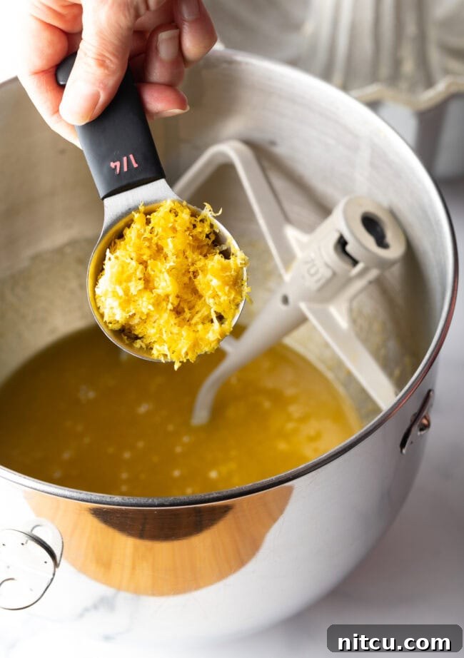 Sun-Kissed Lemon Olive Oil Cake 6 A skilled hand zests a lemon directly into a mixing bowl, capturing every fragrant particle of bright yellow rind, ensuring maximum citrus flavor in the cake batter.