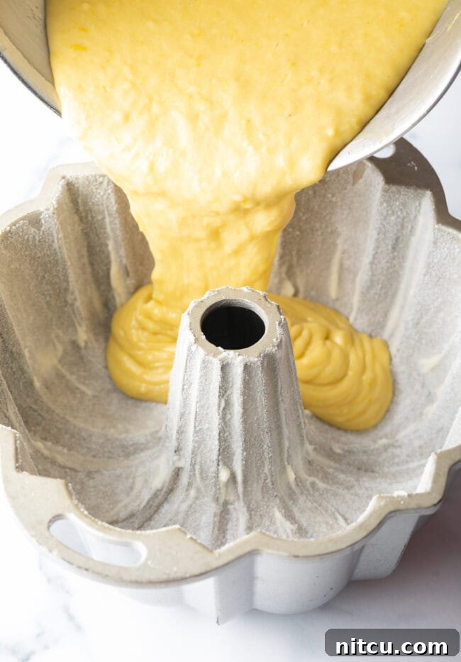 Sun-Kissed Lemon Olive Oil Cake 7 Thick, golden cake batter is carefully poured into a fluted Bundt pan, expertly prepared and ready for baking, promising a beautifully shaped cake.