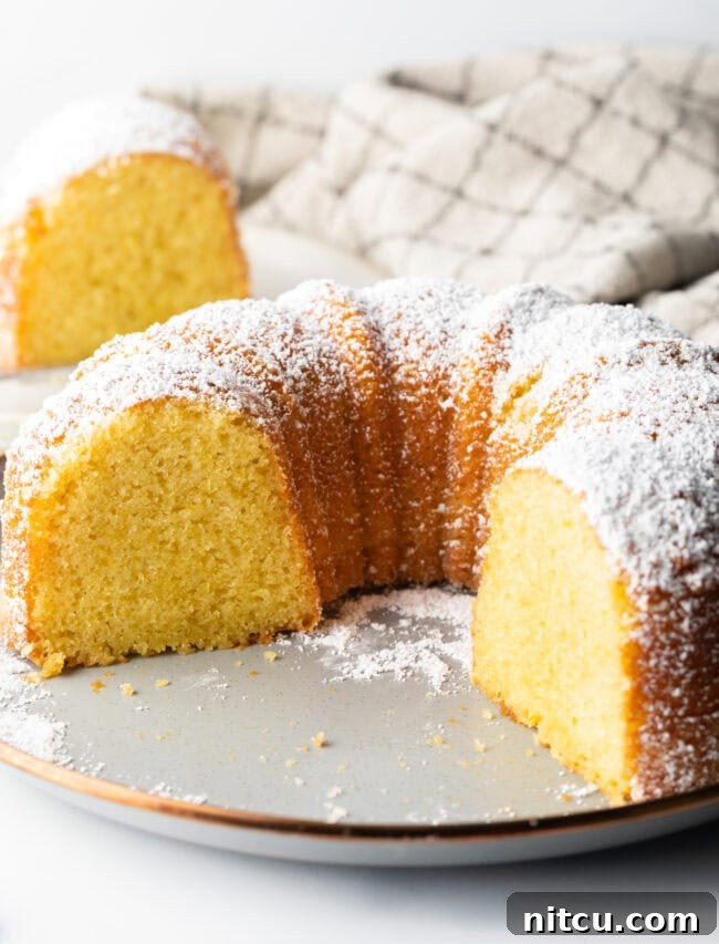 Sun-Kissed Lemon Olive Oil Cake 10 A generous slice of lemon olive oil bundt cake has been removed from the full cake, revealing the incredibly moist, tender, and bright yellow interior crumb.