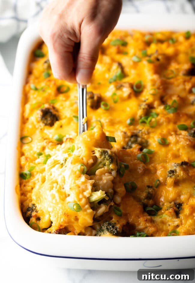 Effortless Cheesy Broccoli Rice Bake 2 Broccoli cheese rice casserole in a white baking dish. A metal spoon is scooping a portion from the dish.