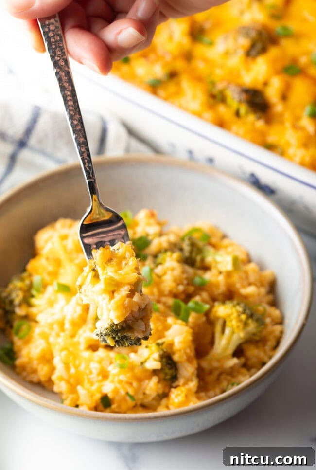 Effortless Cheesy Broccoli Rice Bake 11 Bowl of broccoli, rice, and cheese casserole. There is a fork in the bowl, taking a portion of rice.