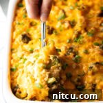 Effortless Cheesy Broccoli Rice Bake 12 Broccoli cheese rice casserole in a white baking dish. A metal spoon is scooping a portion from the dish.