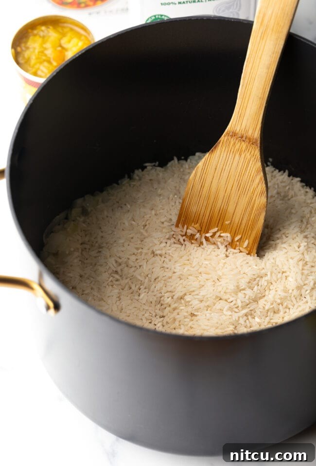 Effortless Cheesy Broccoli Rice Bake 5 White rice in a pot with wooden spoon.
