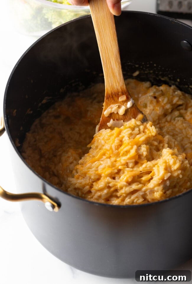 Effortless Cheesy Broccoli Rice Bake 6 Wooden spoon stirring cheese and rice.