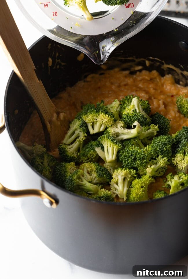 Effortless Cheesy Broccoli Rice Bake 7 Broccoli florets and cheese in a pot with wooden spoon.