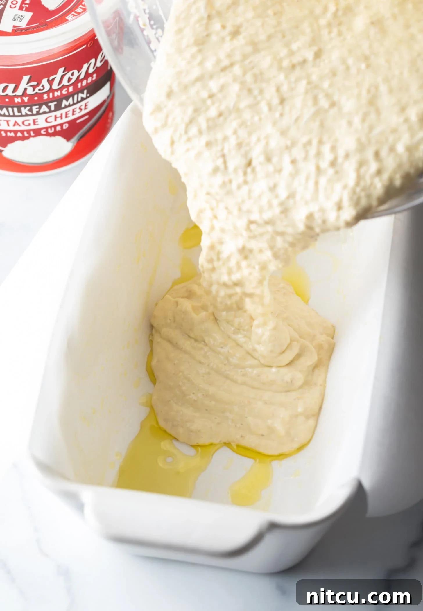 Bread batter being poured into parchment lined loaf pan. 