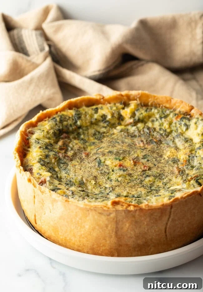 Garden Medley Deep Dish Quiche 2 Baked veggie quiche with a golden deep dish crust on a white round plate, ready to be served.