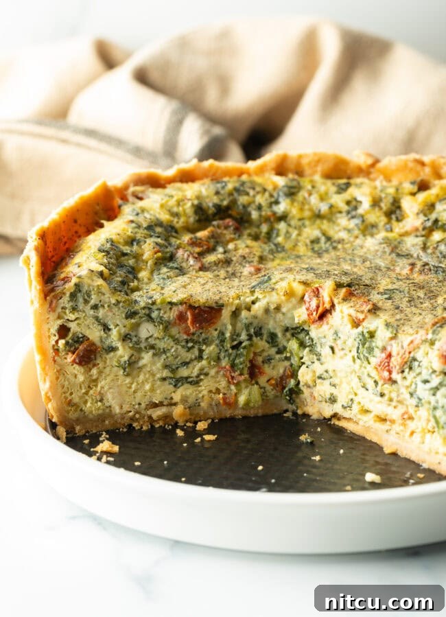 Garden Medley Deep Dish Quiche 11 A beautifully baked deep dish veggie quiche on a white plate, with a large section removed to reveal the rich, vegetable-filled interior and perfectly cooked custard.