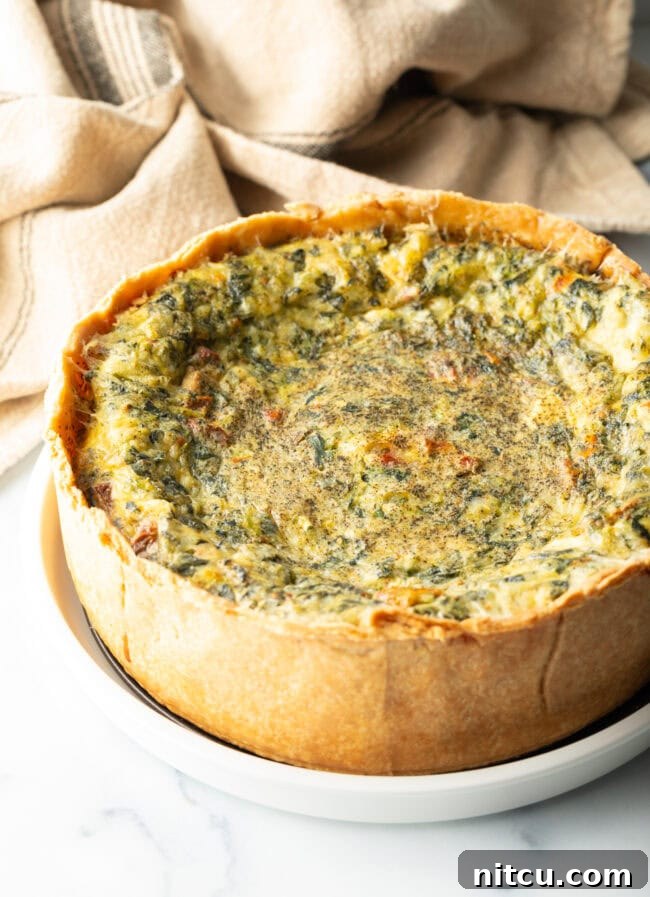 Garden Medley Deep Dish Quiche 10 A perfectly baked deep dish veggie quiche with a golden-brown crust, presented on a pristine white round plate, showcasing its rustic elegance.