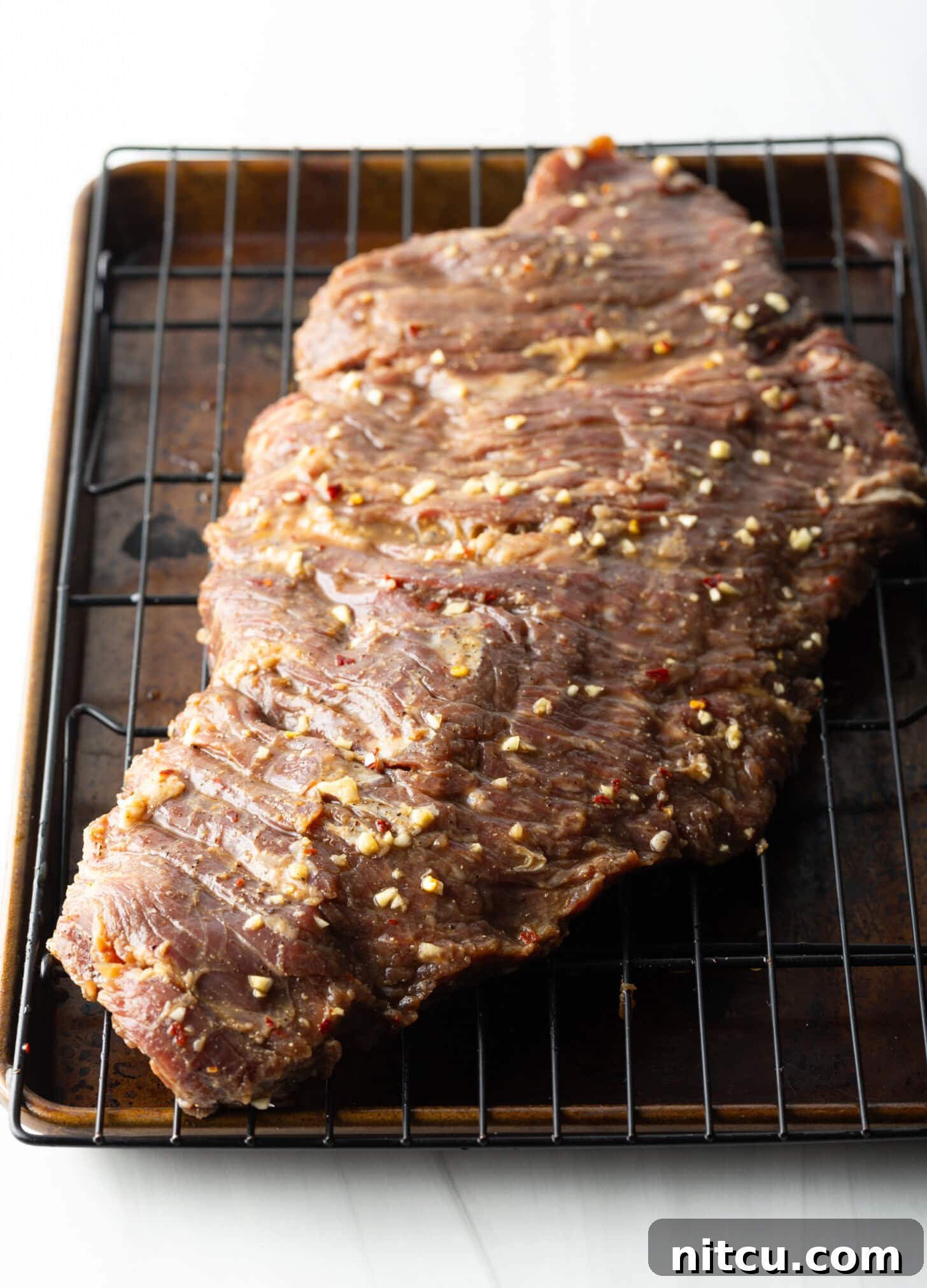 Thin Skirt Steak Delights 6 Raw large section of marinated beef on a wire rack.