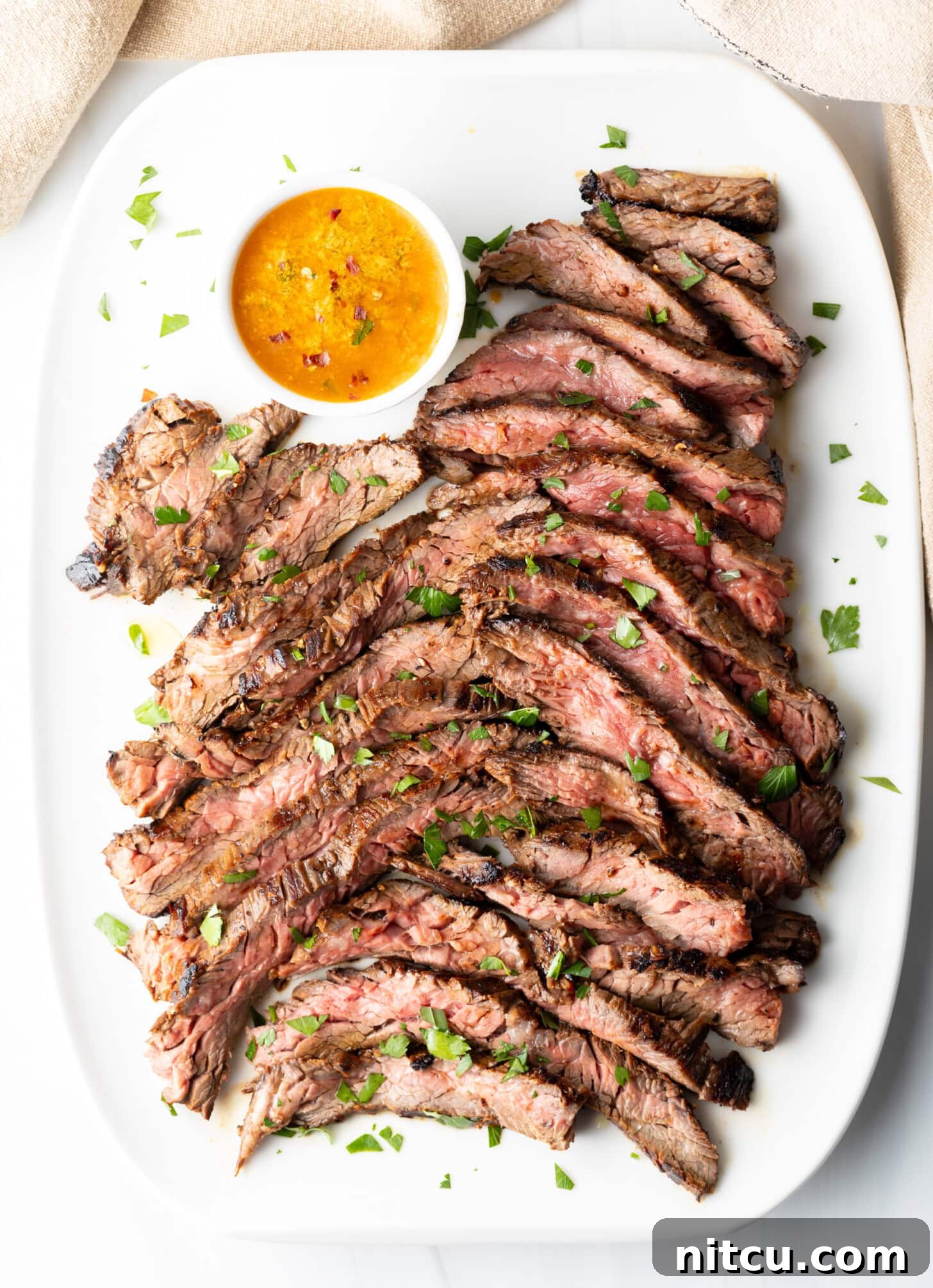 Thin Skirt Steak Delights 9 Thin slices of Bavette steak on a white serving platter with a ramekin of cowboy butter to the side.