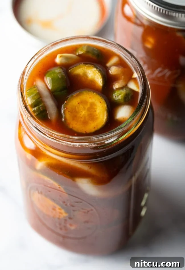 Chamoy Drenched Pickles 2 Two glass jars filled with cucumber slices and chamoy seasonings.